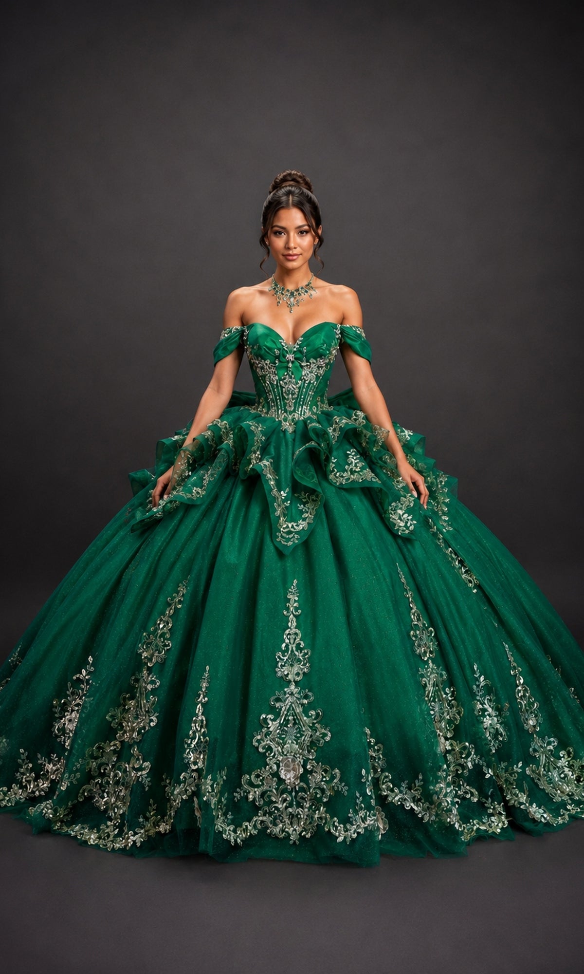 A woman wearing the Quinceanera Dress 5198 by Dancing Queen in hunter green—an elaborate ball gown featuring a corset bodice, off-the-shoulder sleeves, and silver floral embroidery—stands against a plain dark background.